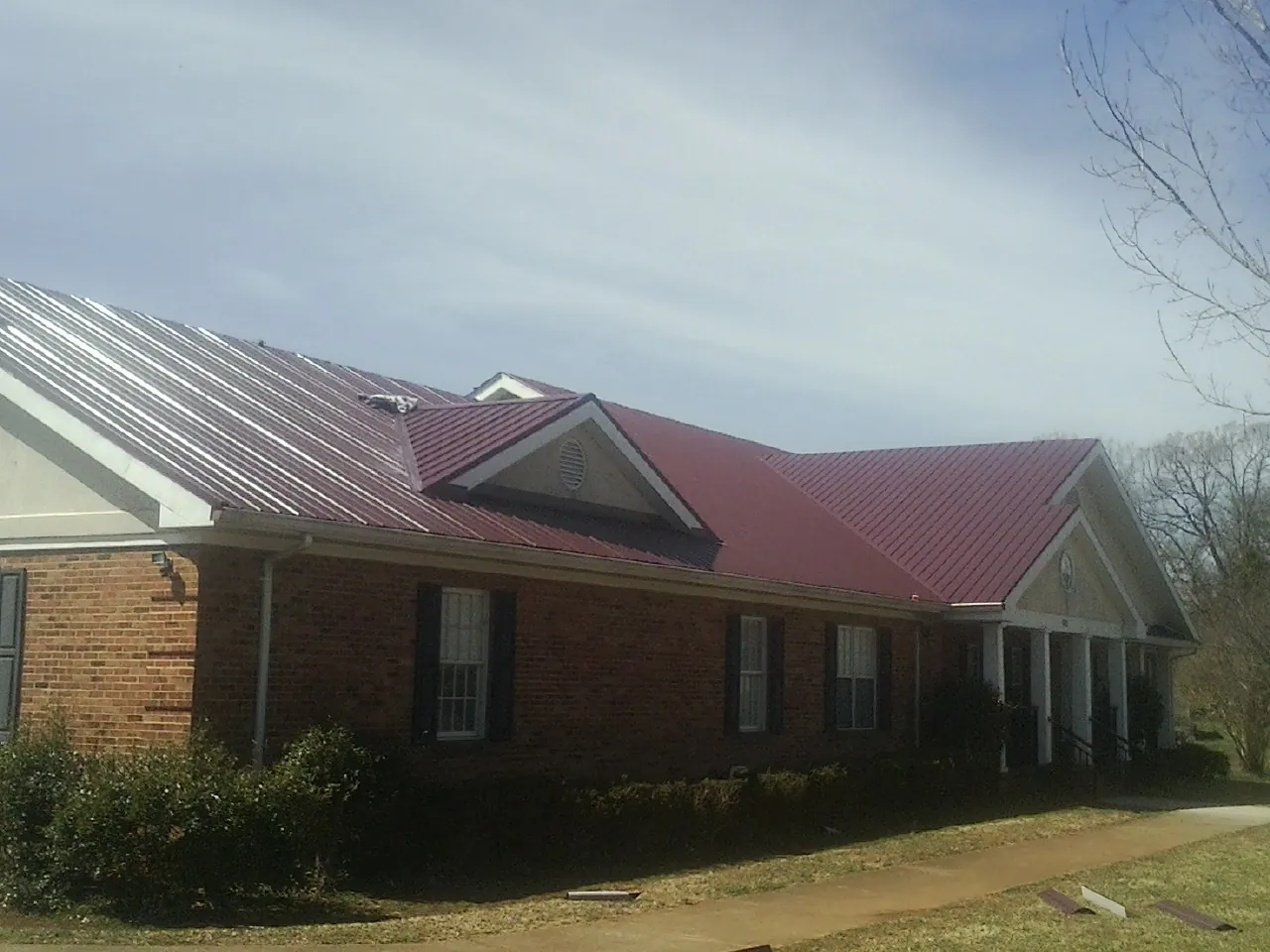 Red metal roof with gabled entries on a long brick building, from a Hail Damage Roof Repair job in Fairmount