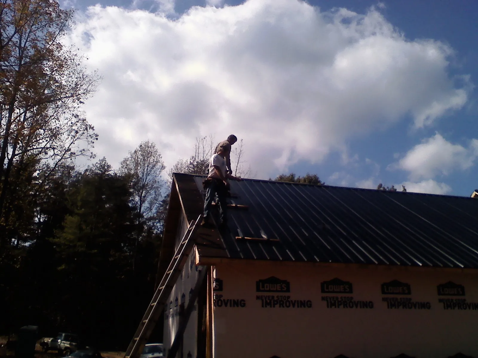 Roofer fastening dark metal panels high against a cloudy sky, from a Roof Inspection job in Fairmount