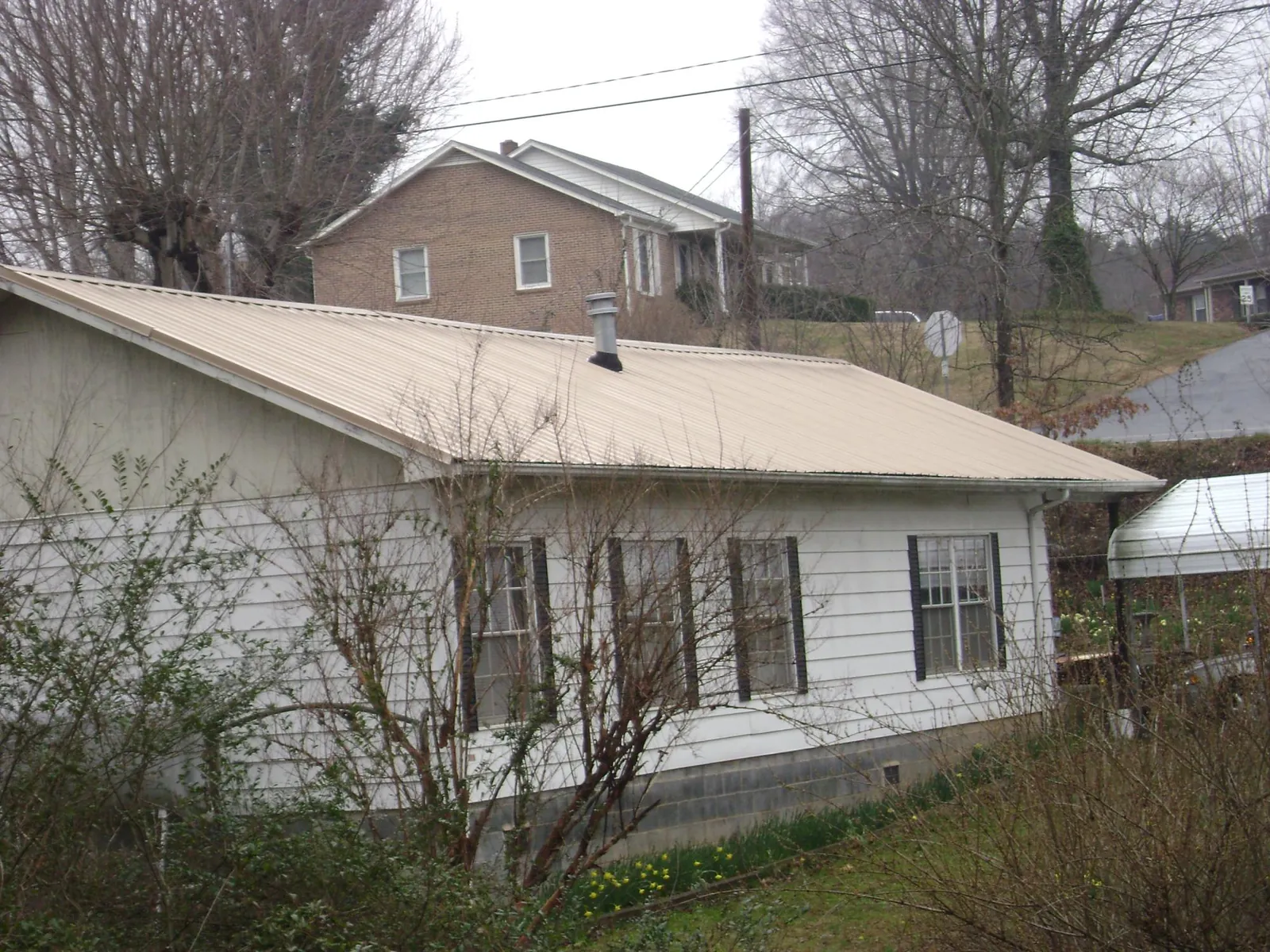 Tan metal roof on a white sided house set into a hillside — Commercial Roofing by Roofing Brothers in Fairmount